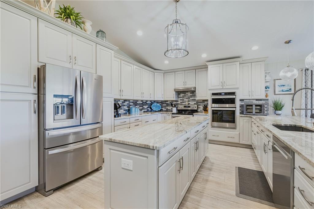 Gourmet kitchen featuring a large central island, light-toned cabinetry, stainless steel appliances including a built-in oven and microwave, and a decorative tile backsplash