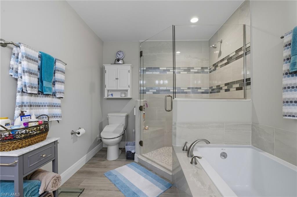 Contemporary bathroom with a glass-enclosed shower, a built-in soaking tub, wood-finish flooring, a wall-mounted cabinet, and recessed lighting