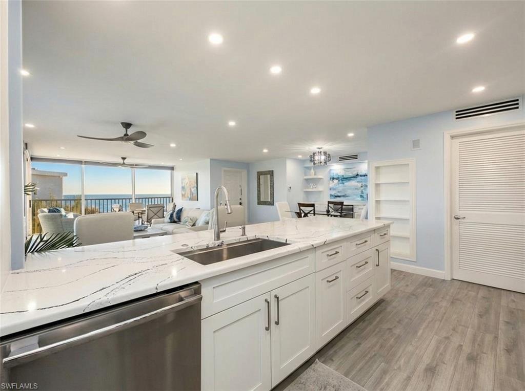 Kitchen featuring stainless steel dishwasher, light stone counters, white cabinetry, light wood-style flooring, and open floor plan