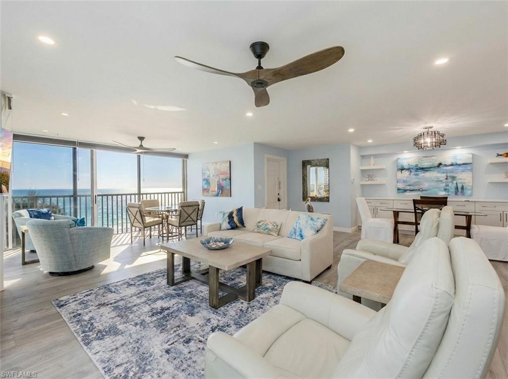 Living area with wood finished floors, floor to ceiling windows, a ceiling fan, hanging lights, and a water view