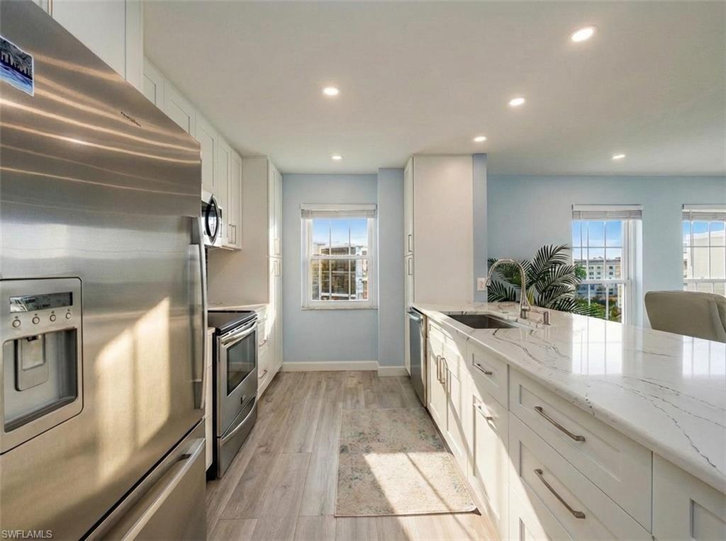 Kitchen featuring stainless steel appliances, white cabinets, light stone counters, light wood finished floors, and recessed lighting