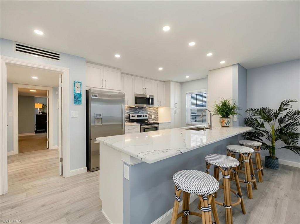 Kitchen with stainless steel appliances, light stone counters, white cabinetry, light wood-style flooring, and a breakfast bar area
