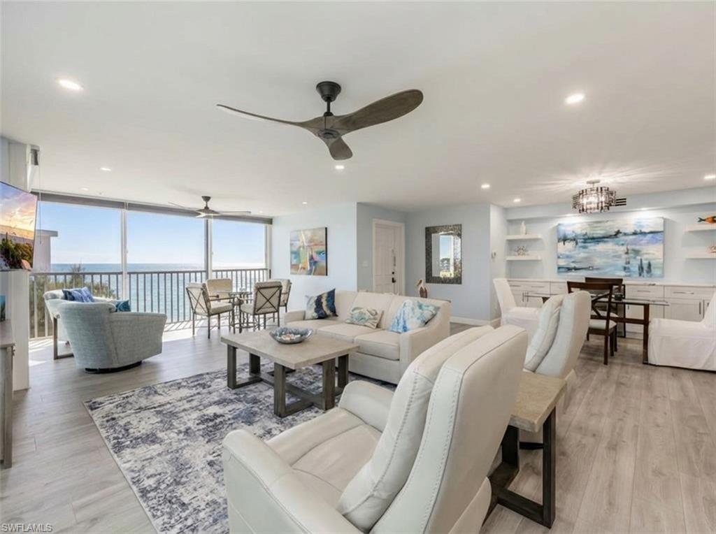 Living area featuring light wood-style flooring, floor to ceiling windows, hanging lights, a ceiling fan, and a water view