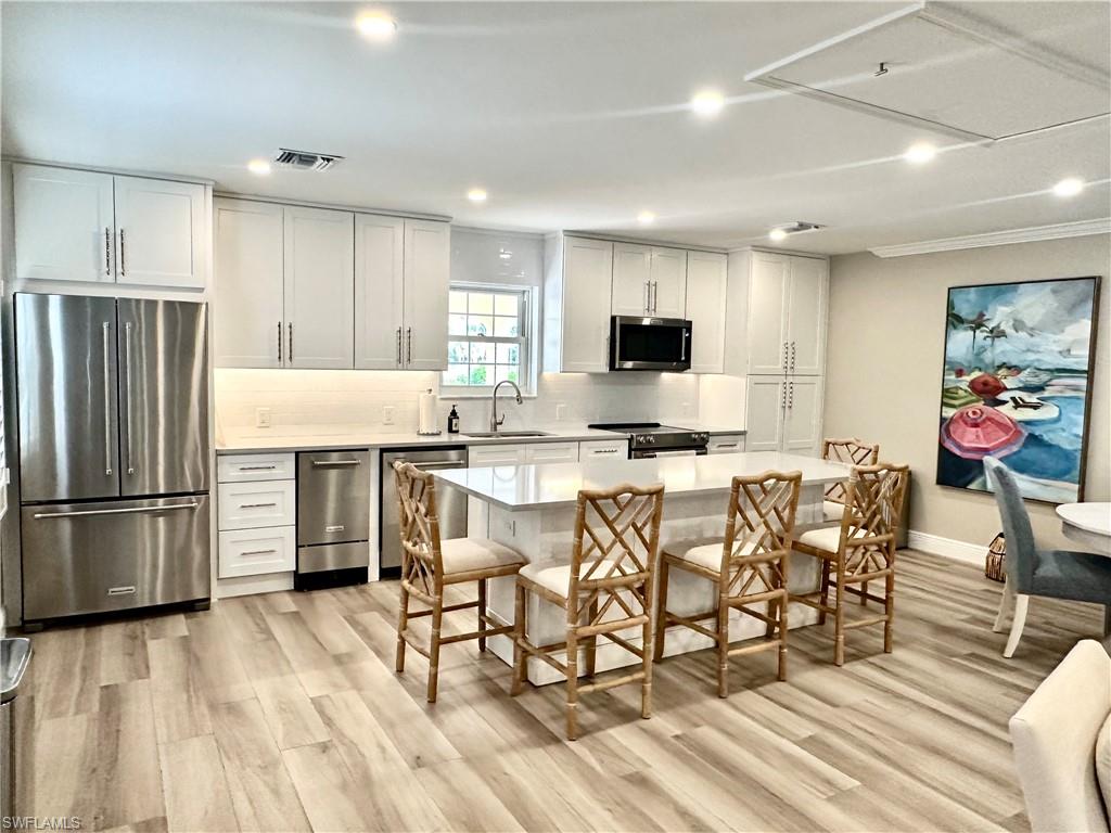 Kitchen with stainless steel appliances, white cabinets, light wood finished floors, recessed lighting, and ornamental molding