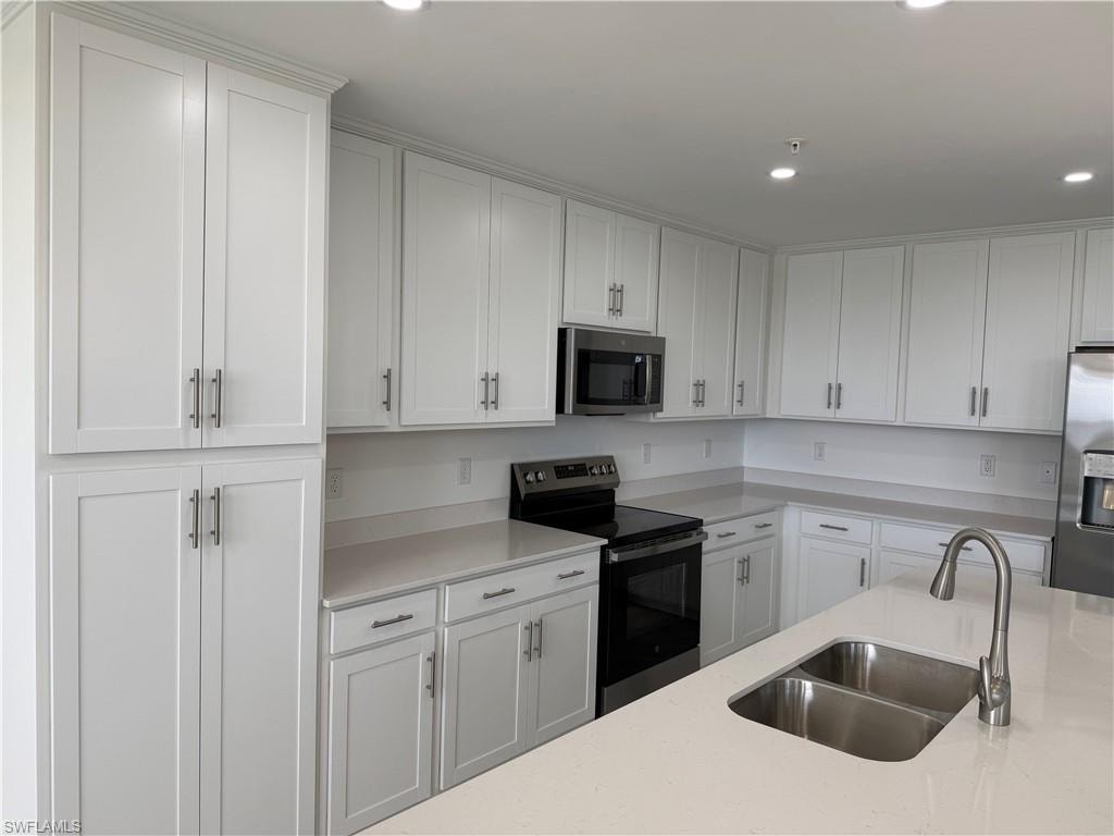 Contemporary kitchen featuring extensive white cabinetry, light countertops, stainless steel appliances, a double basin sink, and recessed lighting