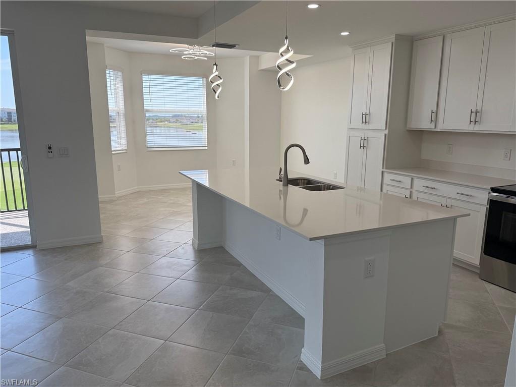 Open-concept kitchen featuring a large central island with a double basin sink, white cabinetry with silver hardware, light-toned countertops, and contemporary pendant lighting
