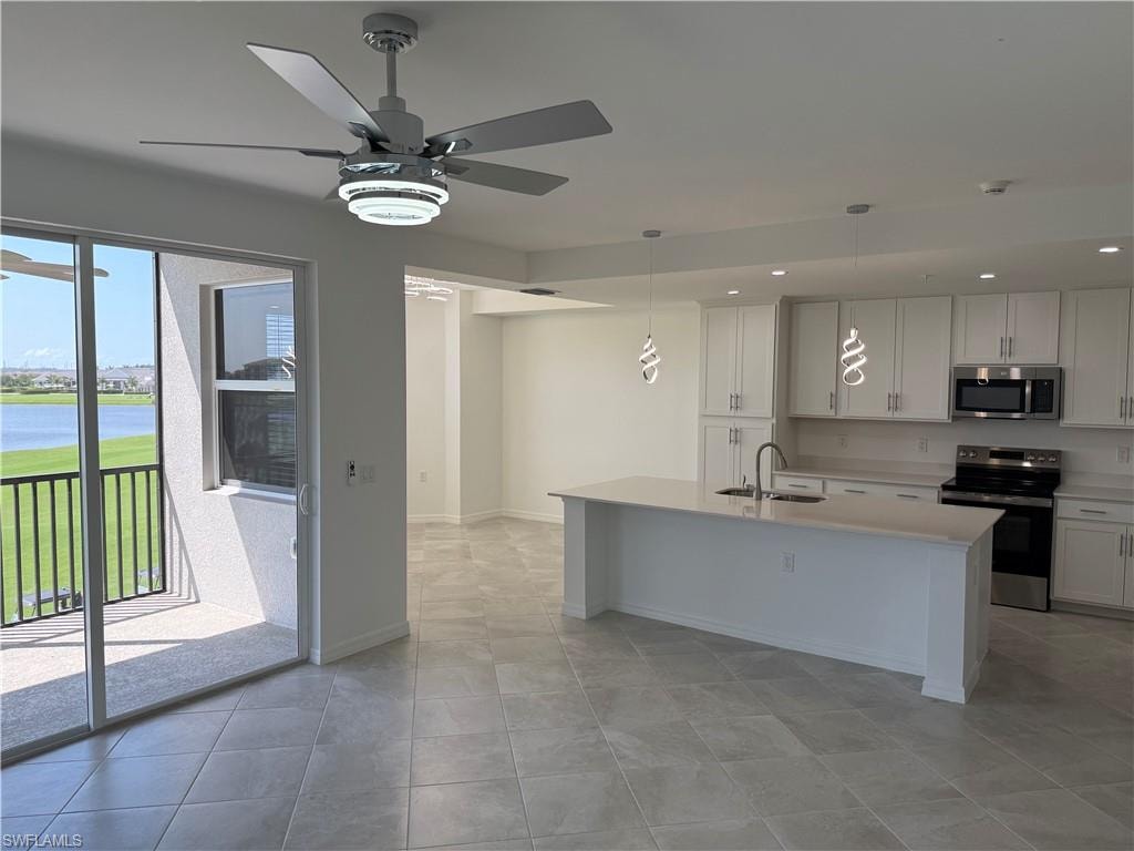 Open-concept kitchen, dining and living area featuring a large center island, white cabinetry, stainless steel appliances, and gray tile flooring