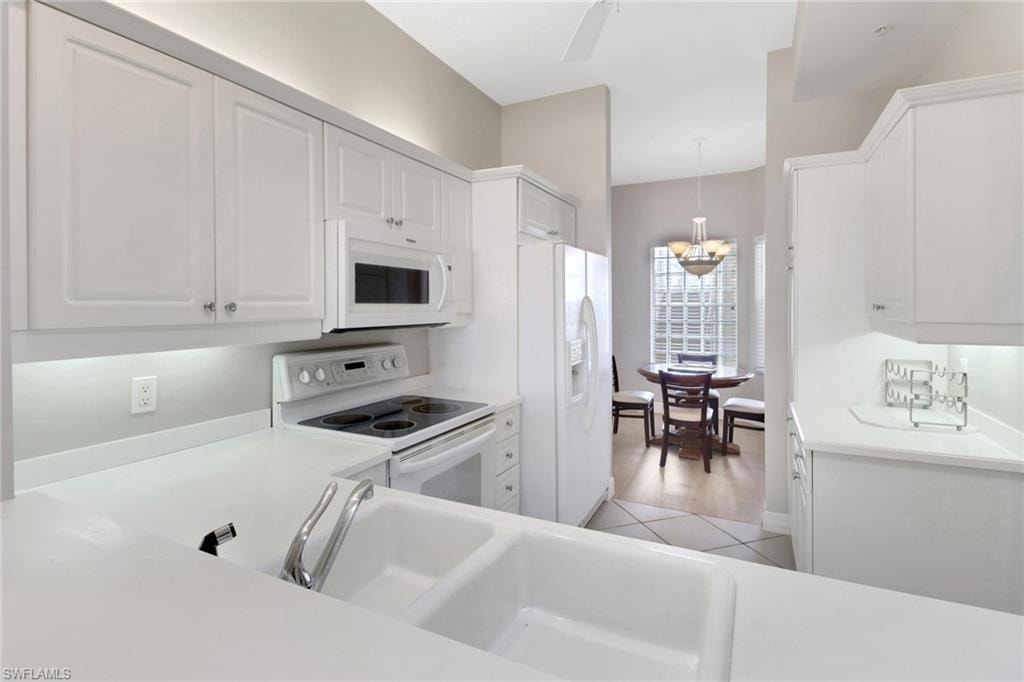 Kitchen featuring white appliances, white cabinets, light countertops, and decorative light fixtures