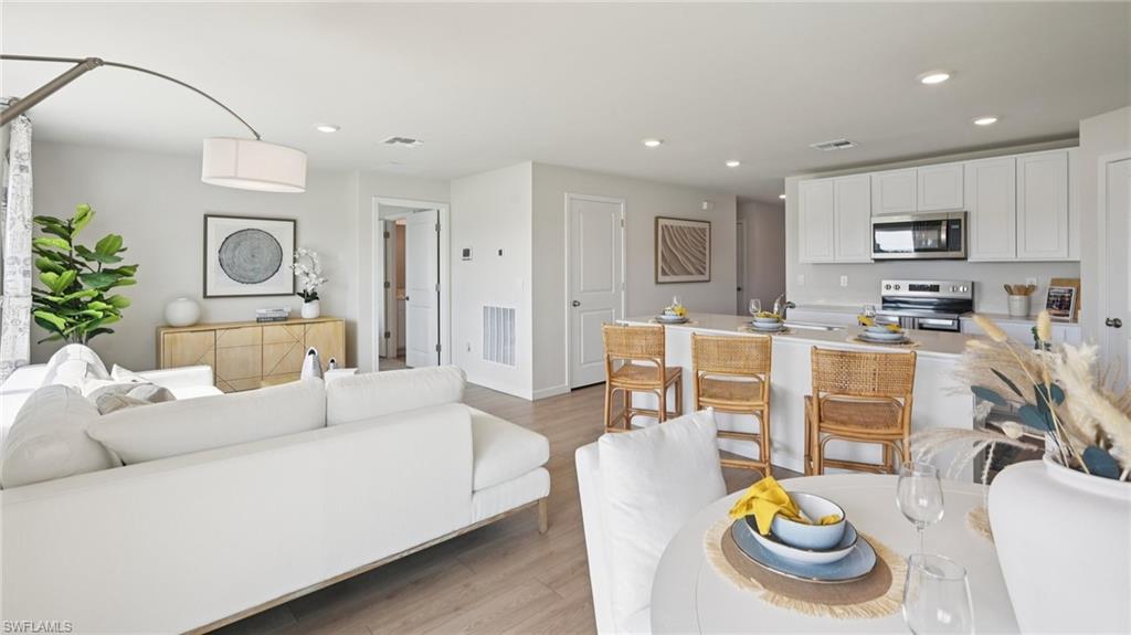 Model Home. The property features an open-concept living area with light-colored flooring, a kitchen with white cabinetry and stainless steel appliances, and a breakfast bar with seating