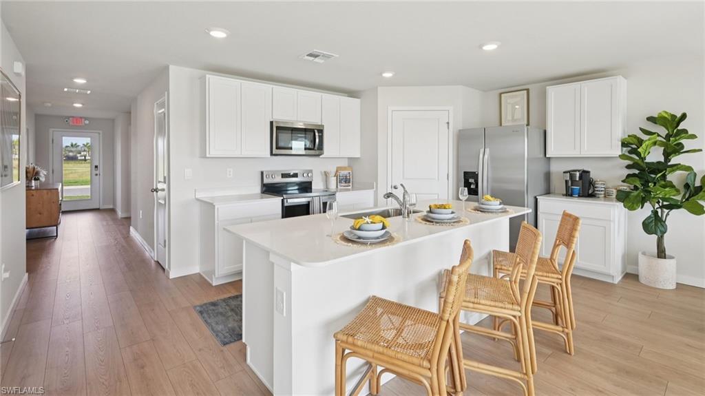 Model Home. The kitchen features a large island with a sink, white cabinetry, and stainless steel appliances, including an oven, microwave, and refrigerator