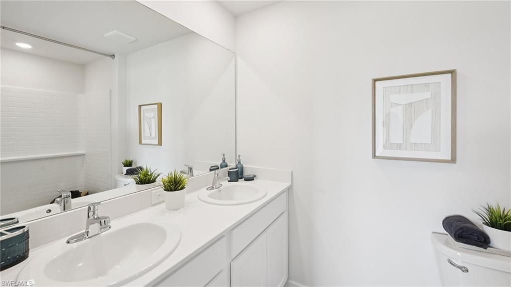 Model Home. Bathroom featuring a large vanity with dual sinks and chrome faucets, a full-width mirror, and white subway tile in the shower area