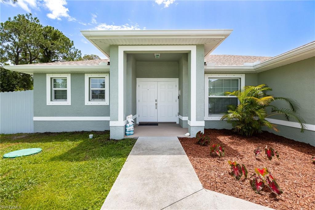 Front exterior featuring a covered entryway with double doors, stucco siding, a concrete walkway, and landscaped garden beds
