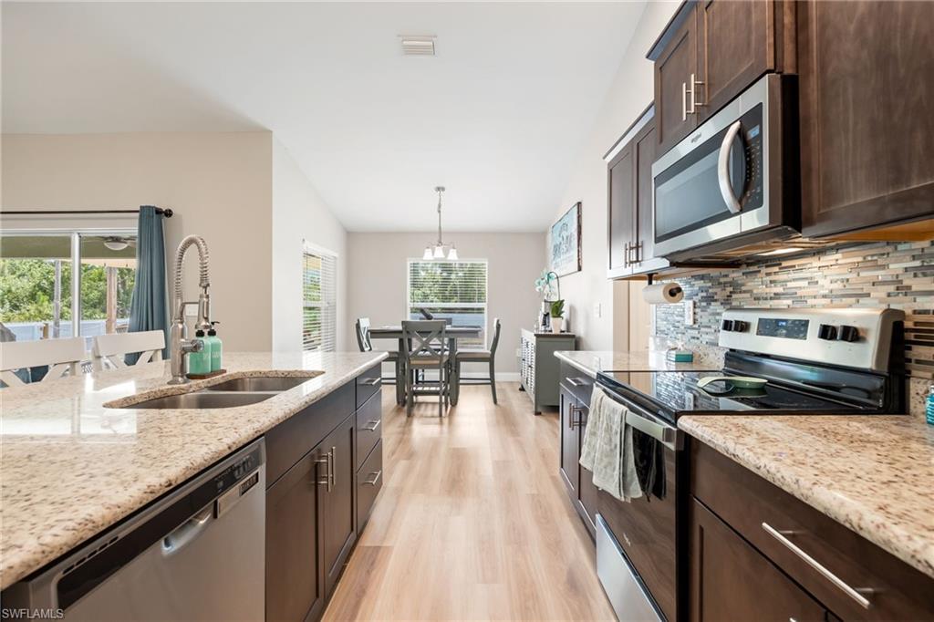 Modern kitchen featuring stainless steel appliances, granite countertops, dark wood cabinetry, a tile backsplash, and wood-finish flooring