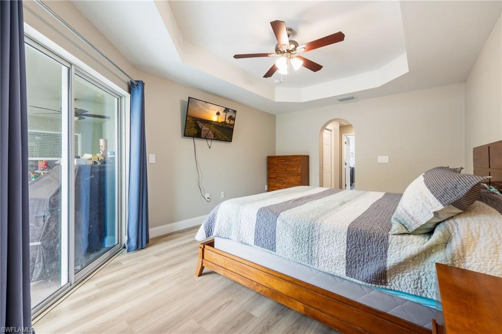 Recessed ceiling with a central fan fixture, wood-finish flooring, sliding glass door access to an exterior space, and an arched doorway leading to an additional interior area