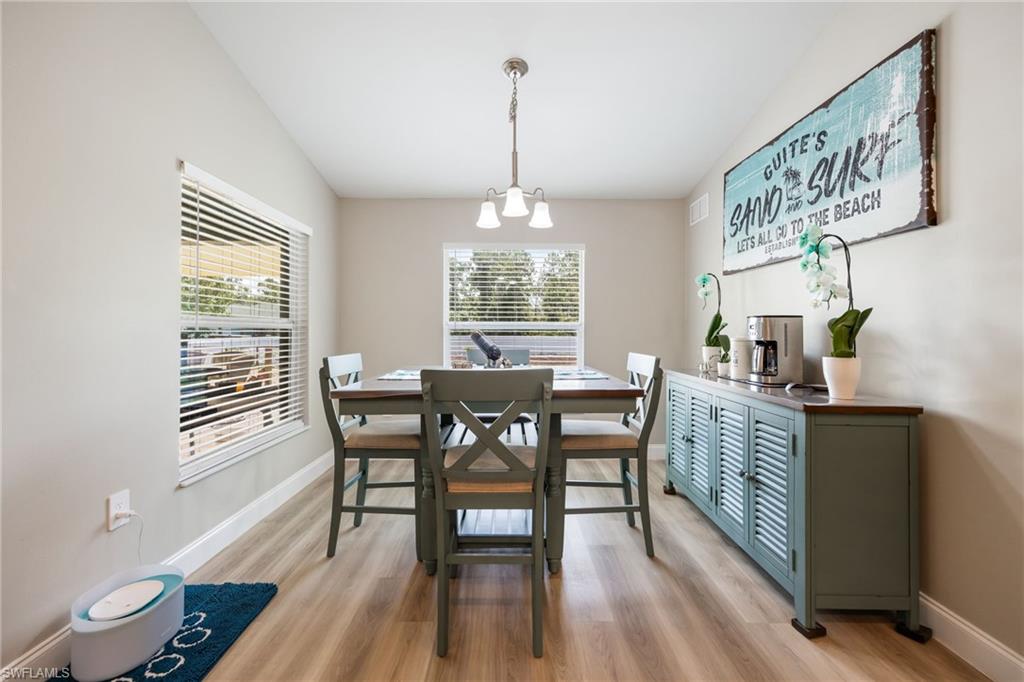 Dining area featuring light wood-finish flooring, two large windows with blinds, a multi-light chandelier, and light neutral wall paint