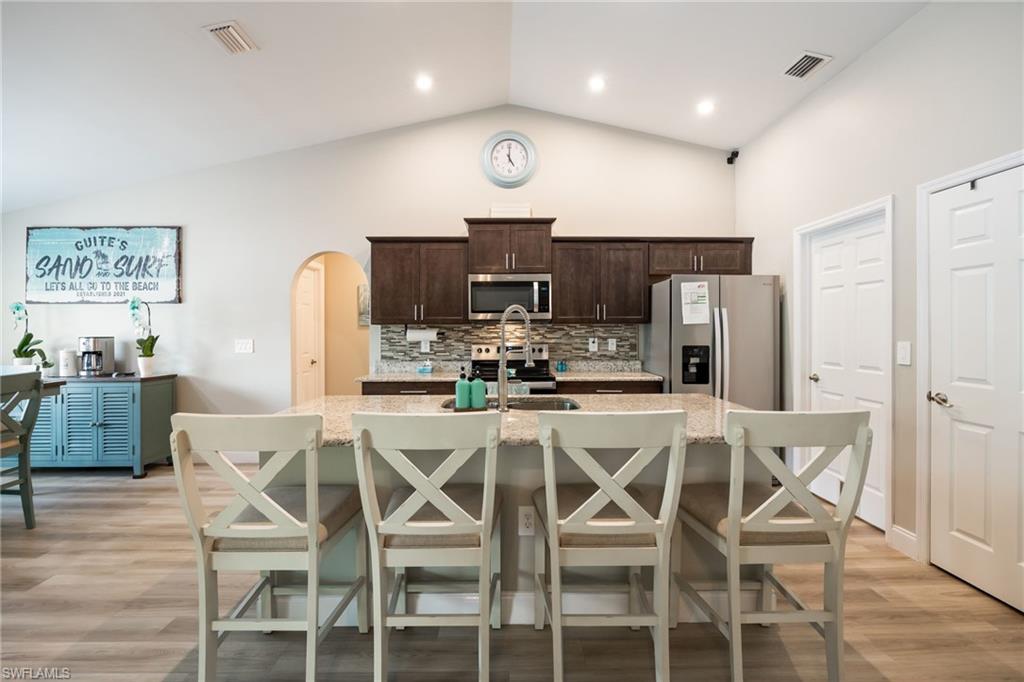 Kitchen featuring a large island with a composite countertop, stainless steel appliances, dark wood cabinetry, and a mosaic tile backsplash