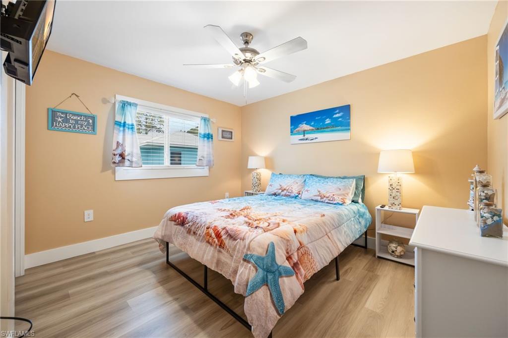 Bedroom featuring wood-finish flooring, a ceiling fan with integrated lighting, a window with white trim, and neutral-toned wall paint