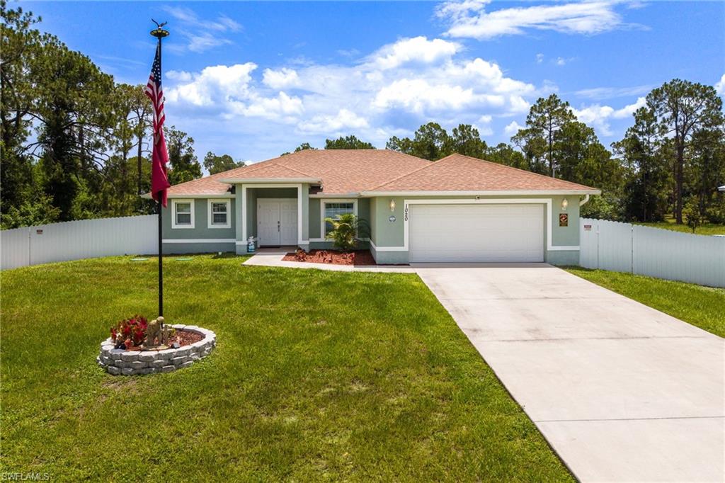 Light green exterior with white trim, featuring a two-car garage, concrete driveway, and a white privacy fence