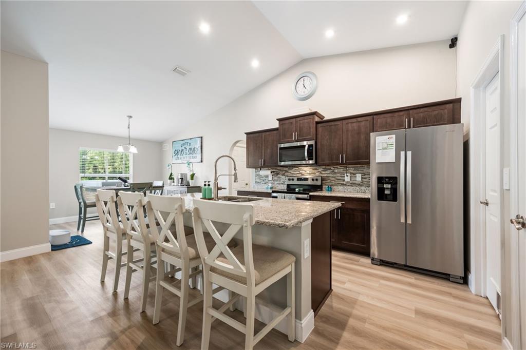 Kitchen featuring wood-finish flooring, dark wood cabinetry, stainless steel appliances, and a granite island with seating