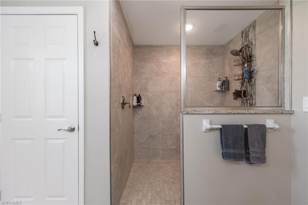 Walk-in shower featuring tiled walls and floor, a glass enclosure, and a partial privacy wall with a stone cap
