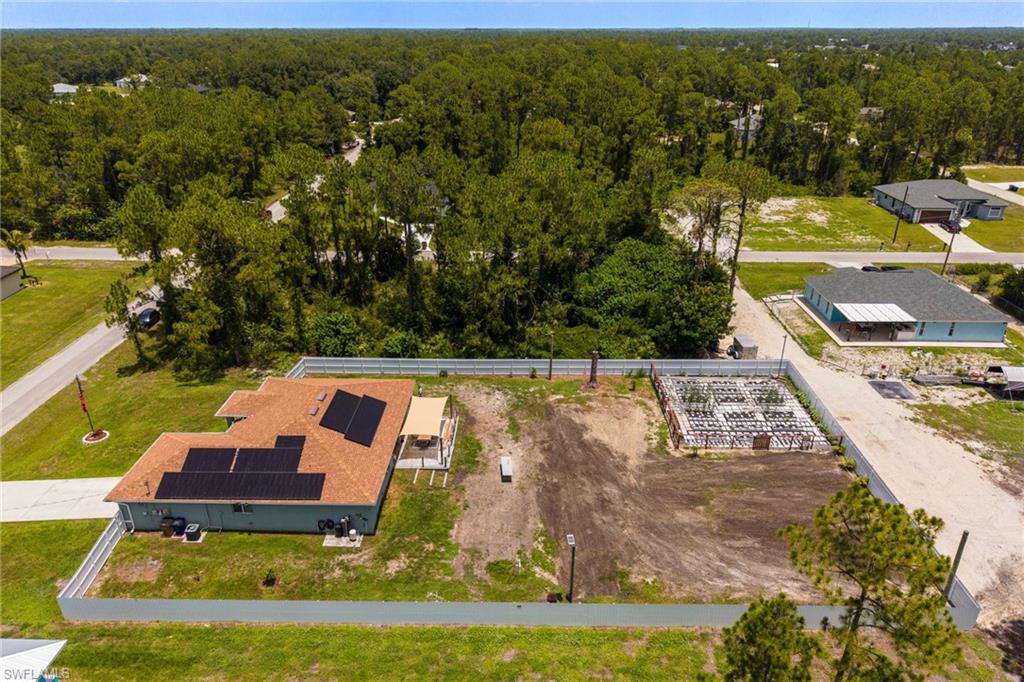 Aerial perspective showcasing a single-story residence with a brown shingle roof, integrated solar panels, and an attached covered patio