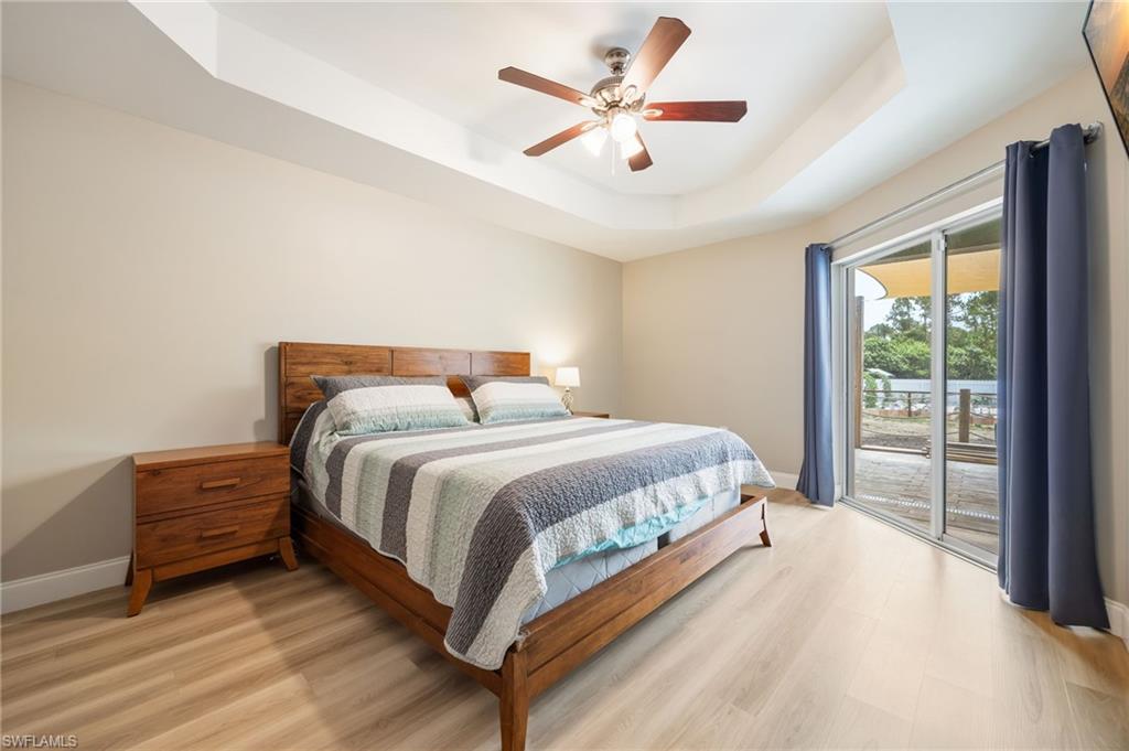 Recessed tray ceiling with ceiling fan and light kit, wood-finish flooring, and sliding glass door leading to an outdoor space