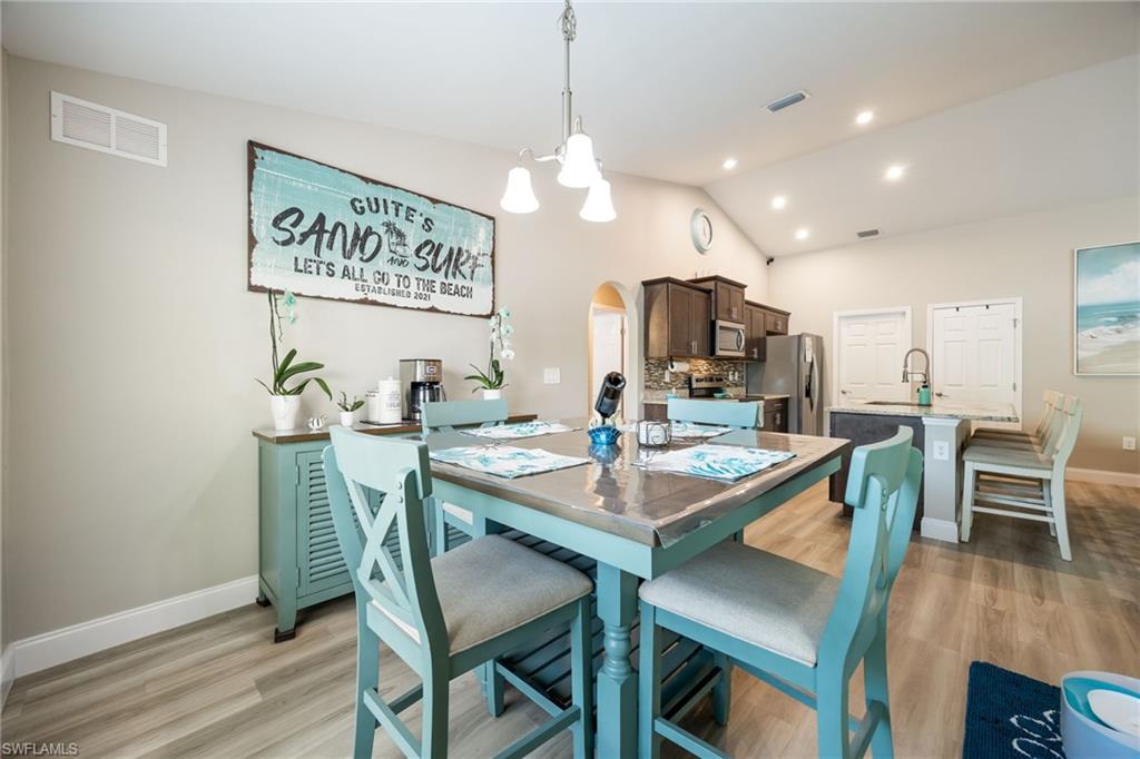 Open-concept living area featuring vaulted ceilings, recessed lighting, wood-finish flooring, a kitchen island with a sink, and dark wood cabinetry