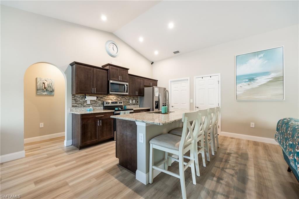 Kitchen featuring wood-finish flooring, vaulted ceiling, recessed lighting, dark wood cabinetry, and a granite-topped island with seating