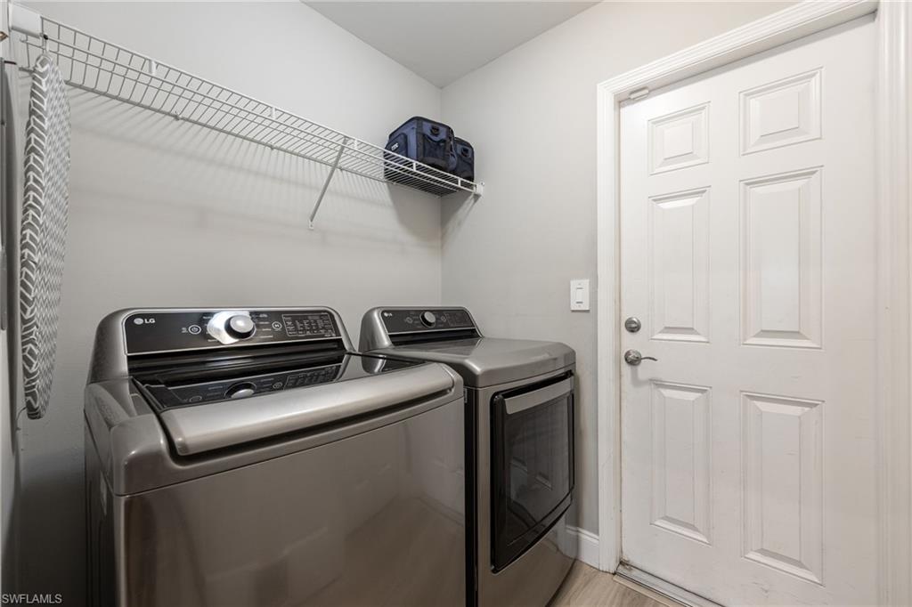 Dedicated utility room featuring light gray walls, wood-finish flooring, a white paneled door with brushed nickel hardware, and an overhead wire shelving unit