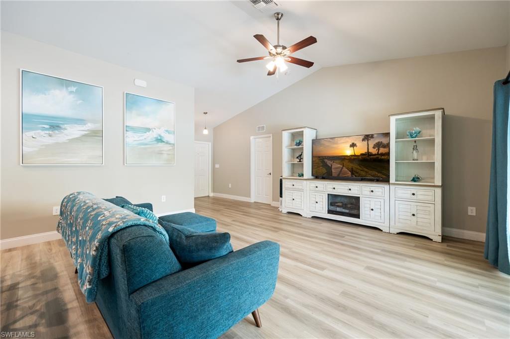 Spacious living area featuring light wood-finish flooring, vaulted ceilings, and a ceiling fan