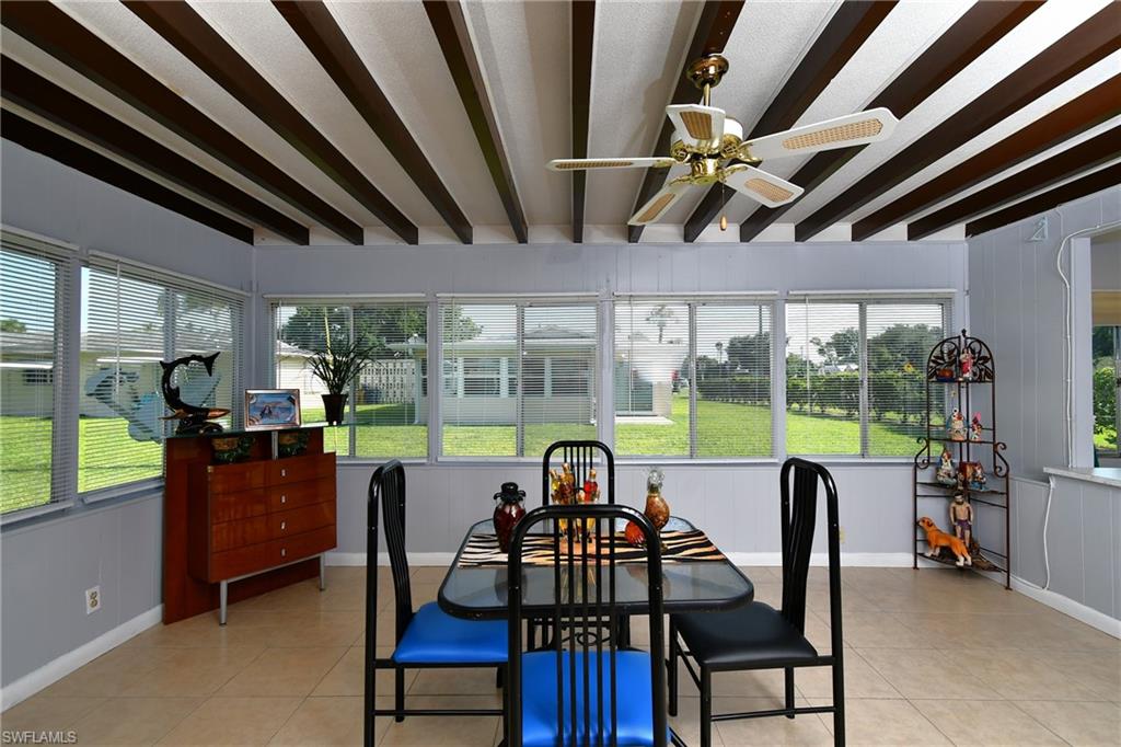 Sunroom featuring exposed ceiling beams, multiple windows, a ceiling fan, and tile flooring