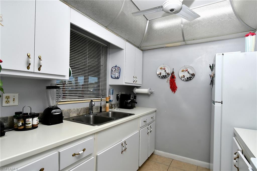 White cabinetry with decorative hardware, a dual basin stainless steel sink, a tile backsplash, and light-colored countertops