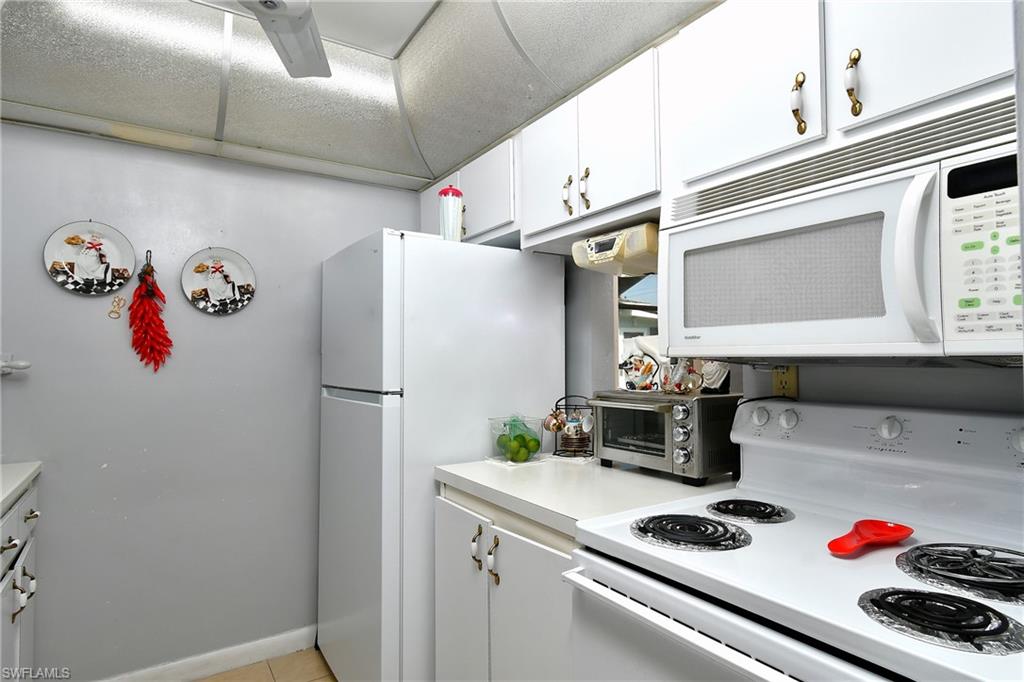 Compact kitchen featuring white cabinetry, white appliances, and light-toned countertops