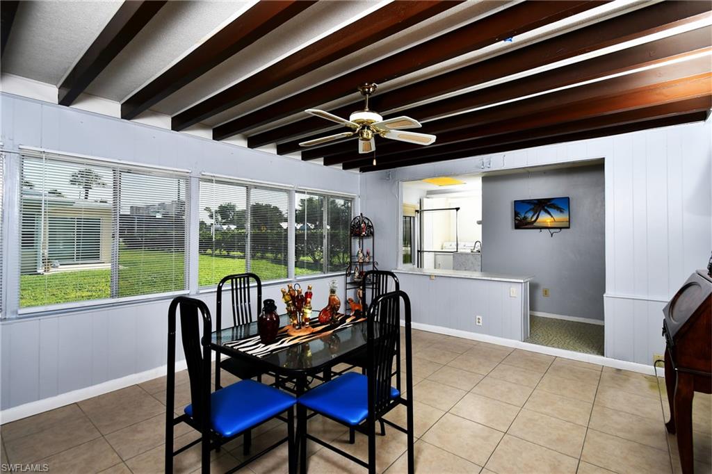 Expansive sunroom featuring full-width windows, exposed wood-beam ceiling, ceiling fan, and tile flooring