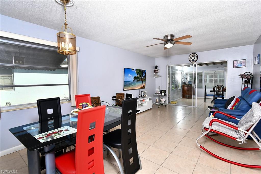 Open-concept living area featuring light-toned tile flooring, a dining space with a contemporary chandelier, and sliding glass doors leading to an enclosed patio