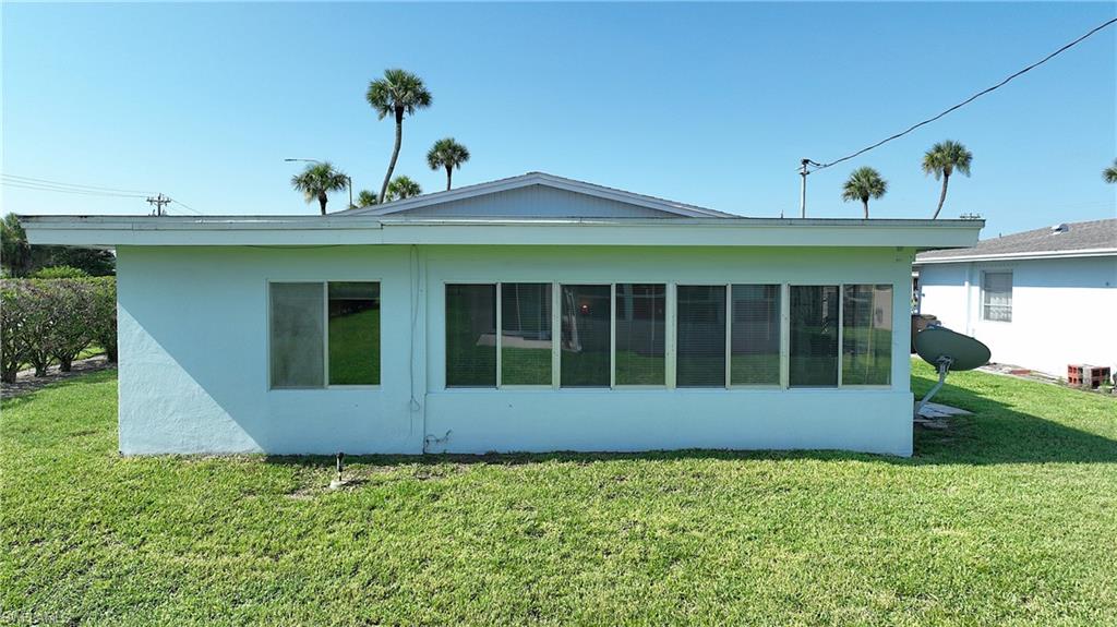 Exterior featuring light blue stucco finish, a covered patio with multiple windows, and a green lawn