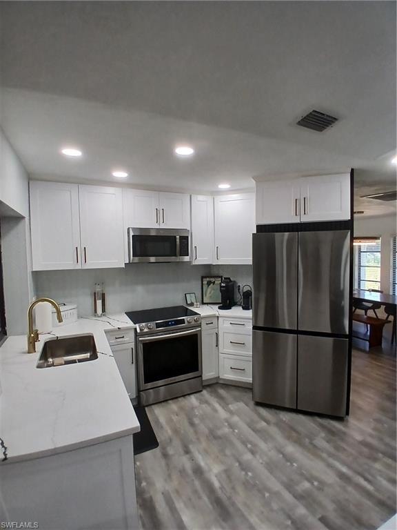 Modern kitchen featuring white shaker cabinetry, stainless steel appliances, a gold-finish faucet, white countertops, and wood-finish flooring