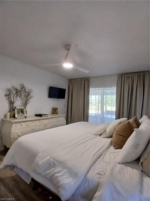 Bedroom featuring a contemporary ceiling fan with integrated lighting, wood-finish flooring, and a window with both sheer and blackout drapery