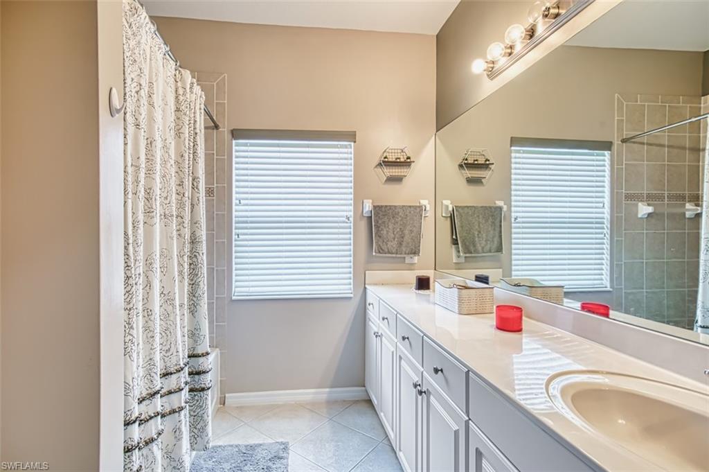 Bathroom featuring a spacious vanity with an integrated sink and extensive countertop space, a large mirror, and a shower with tiled walls
