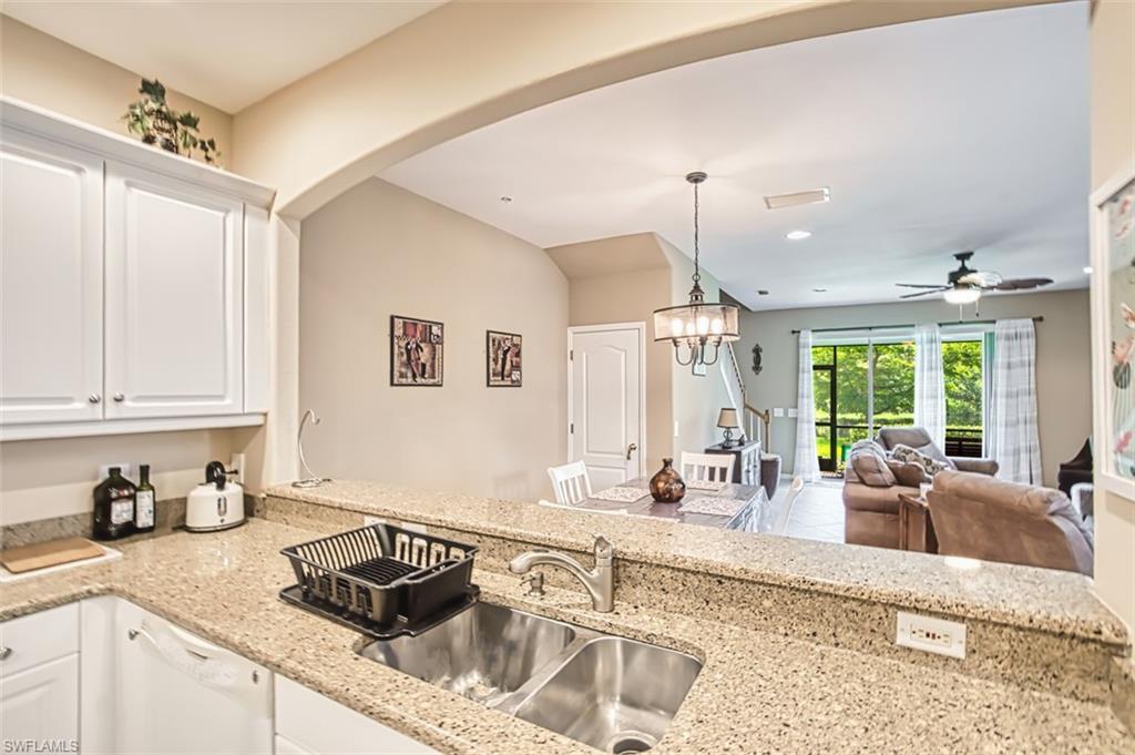Kitchen featuring a double basin stainless steel sink, solid surface countertops, white cabinetry, and an arched pass-through window to the living area