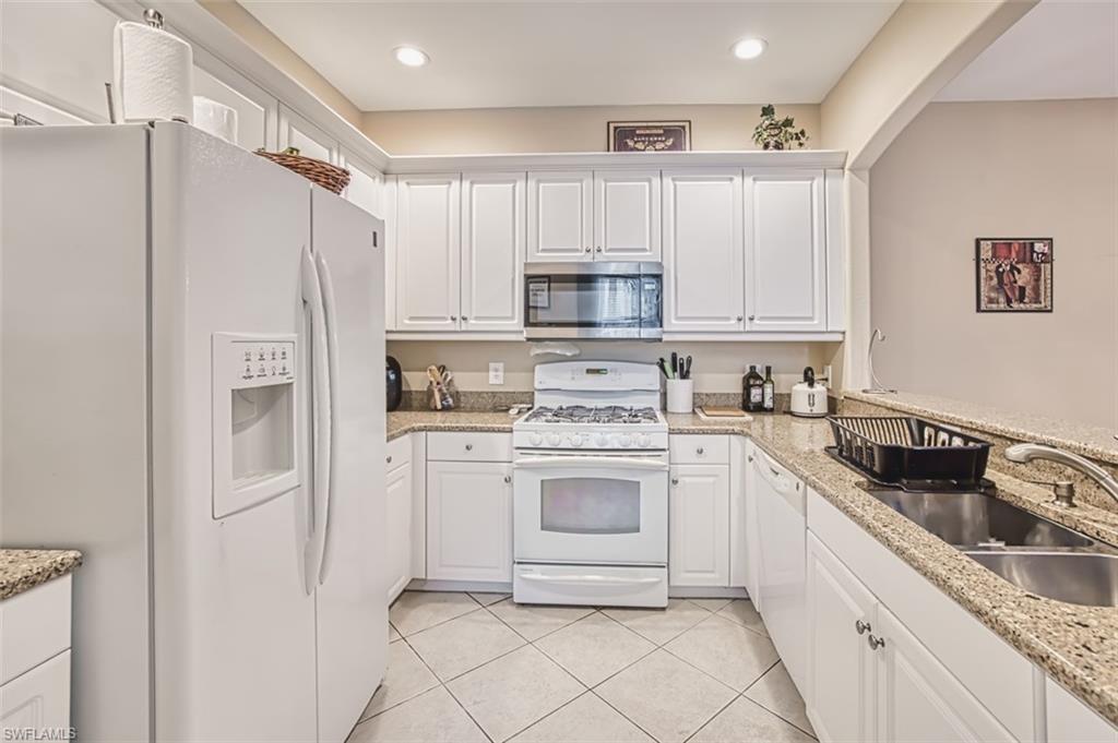 Kitchen featuring white cabinetry, granite-finish countertops, stainless steel microwave, gas range, and a double basin sink