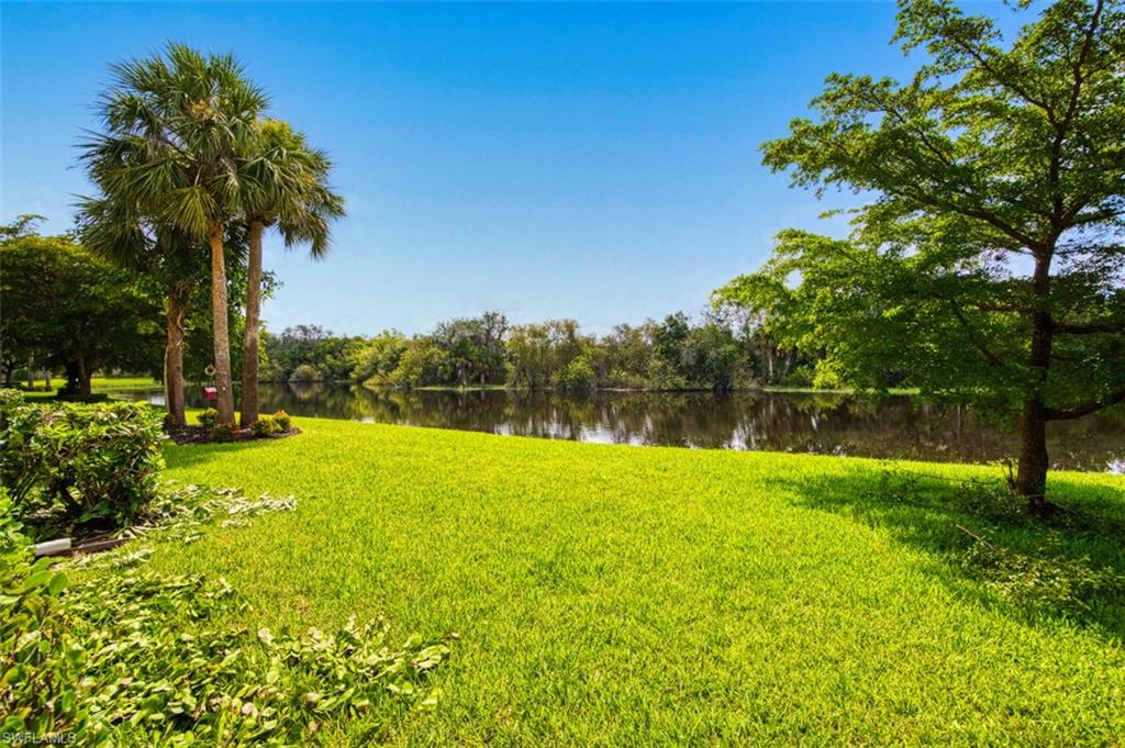 Lush green lawn bordering a tranquil body of water, featuring mature trees and established landscaping under a clear sky