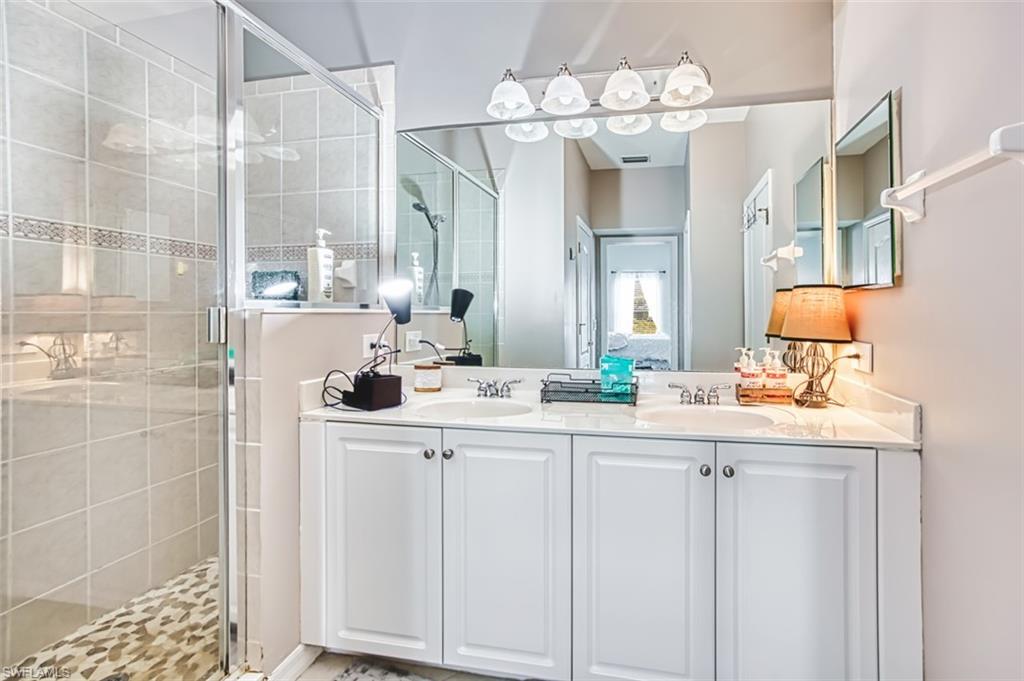 Bathroom featuring a dual vanity with white cabinetry, a large mirror, and a glass-enclosed shower with tiled walls and a decorative accent strip