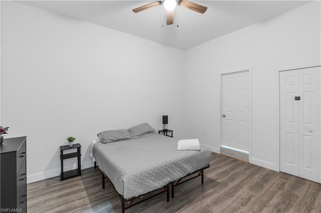 Bright interior space with wood-finish flooring, a ceiling fan, a white panel door, and white bi-fold closet doors