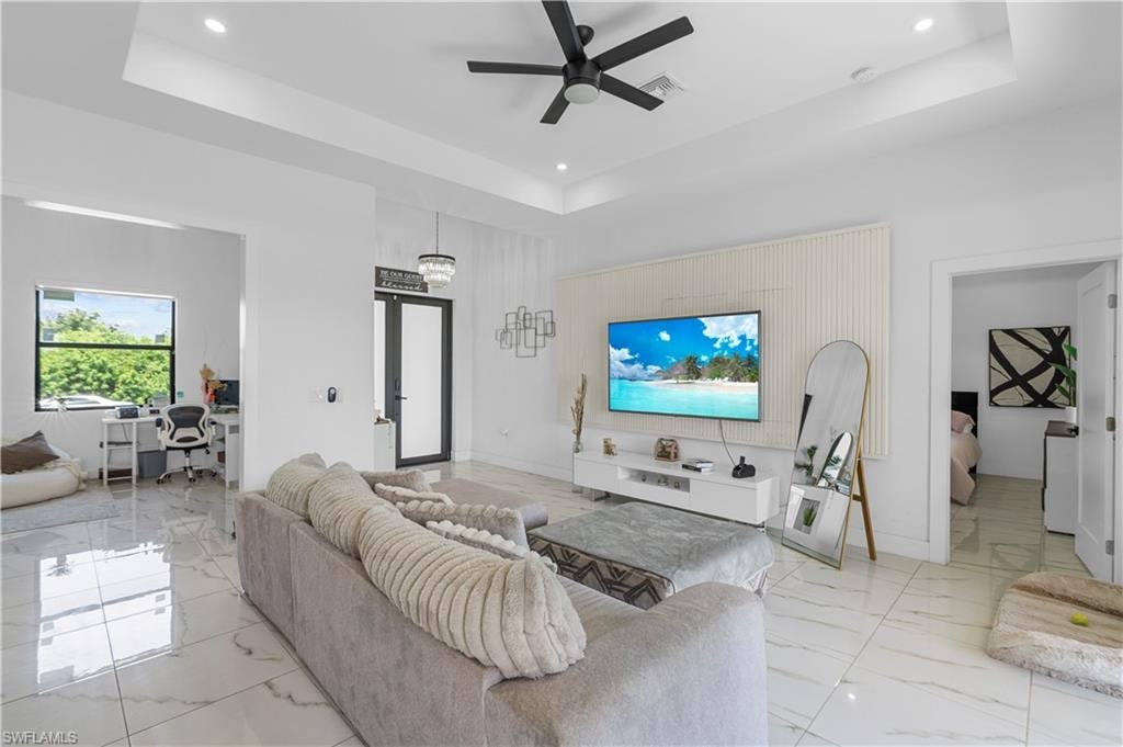 Spacious living area featuring large format white tile flooring, a tray ceiling with recessed lighting, and a black ceiling fan