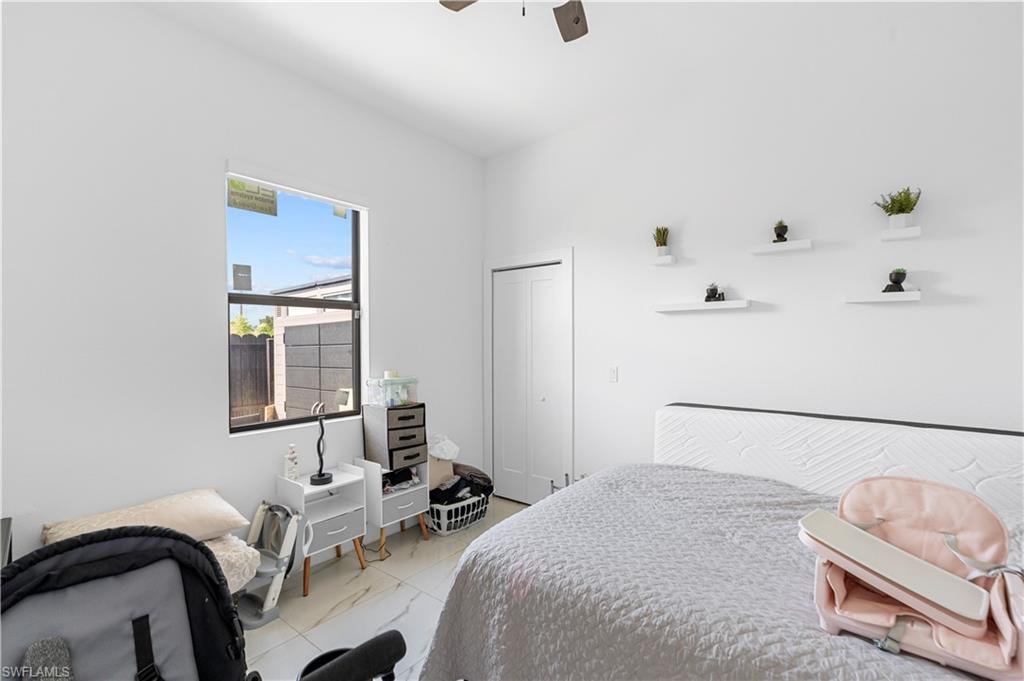 Bright room featuring white walls, a single window, white tiled flooring with a subtle veining pattern, a white ceiling fan, and a white bi-fold closet door