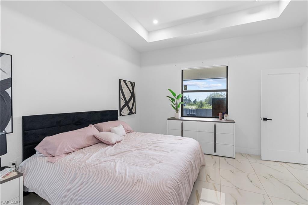 Spacious bedroom featuring a tray ceiling, large window, white interior walls, and tile flooring