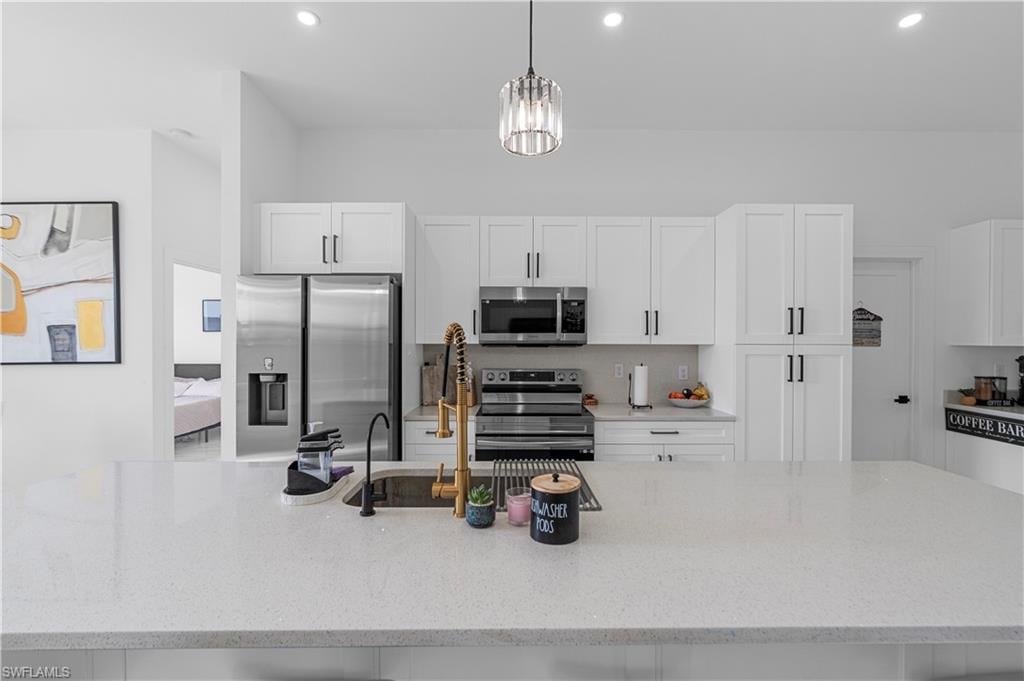 Spacious kitchen featuring an expansive island with a built-in sink and two-tone faucet, white shaker cabinetry with dark hardware, stainless steel appliances, and recessed lighting