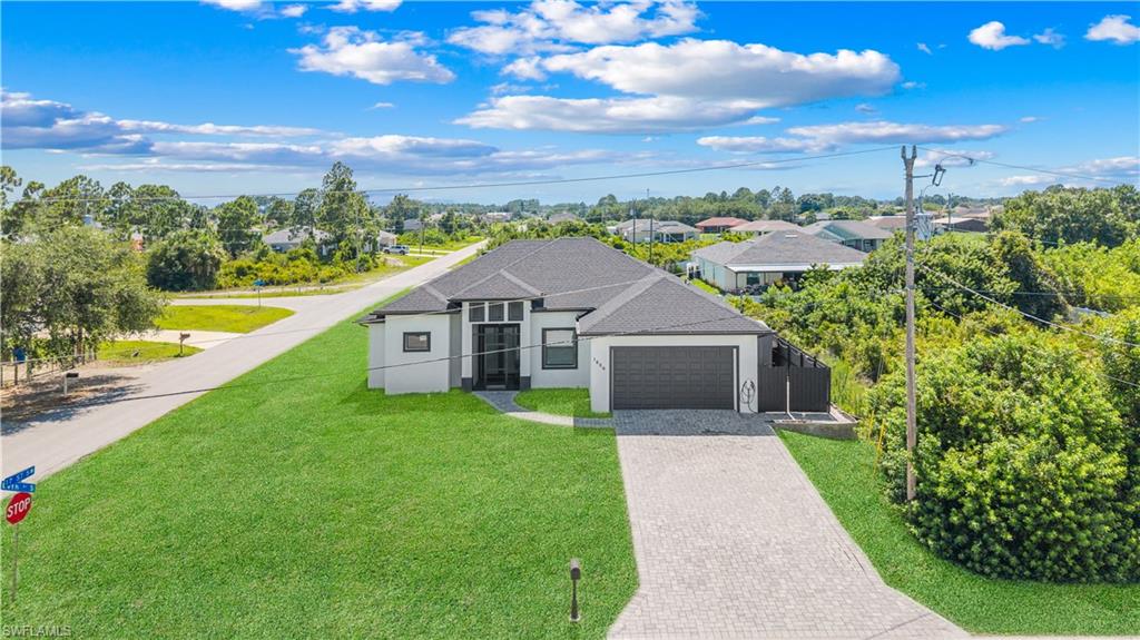 Modern single-story residence featuring a dark gray shingle roof, a two-car garage with a dark gray door, a light gray paved driveway, a manicured green lawn, and a front entry with glass double doors