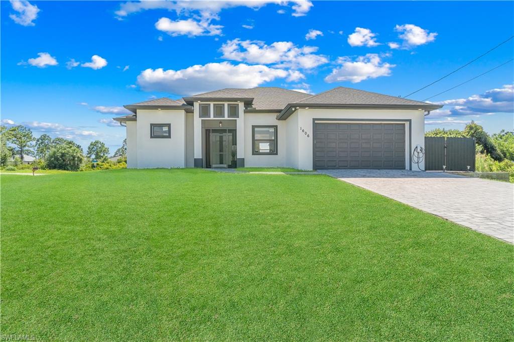 Contemporary single-story residence featuring a smooth stucco exterior, a dark gray overhead garage door, a paved driveway, and an expansive green lawn